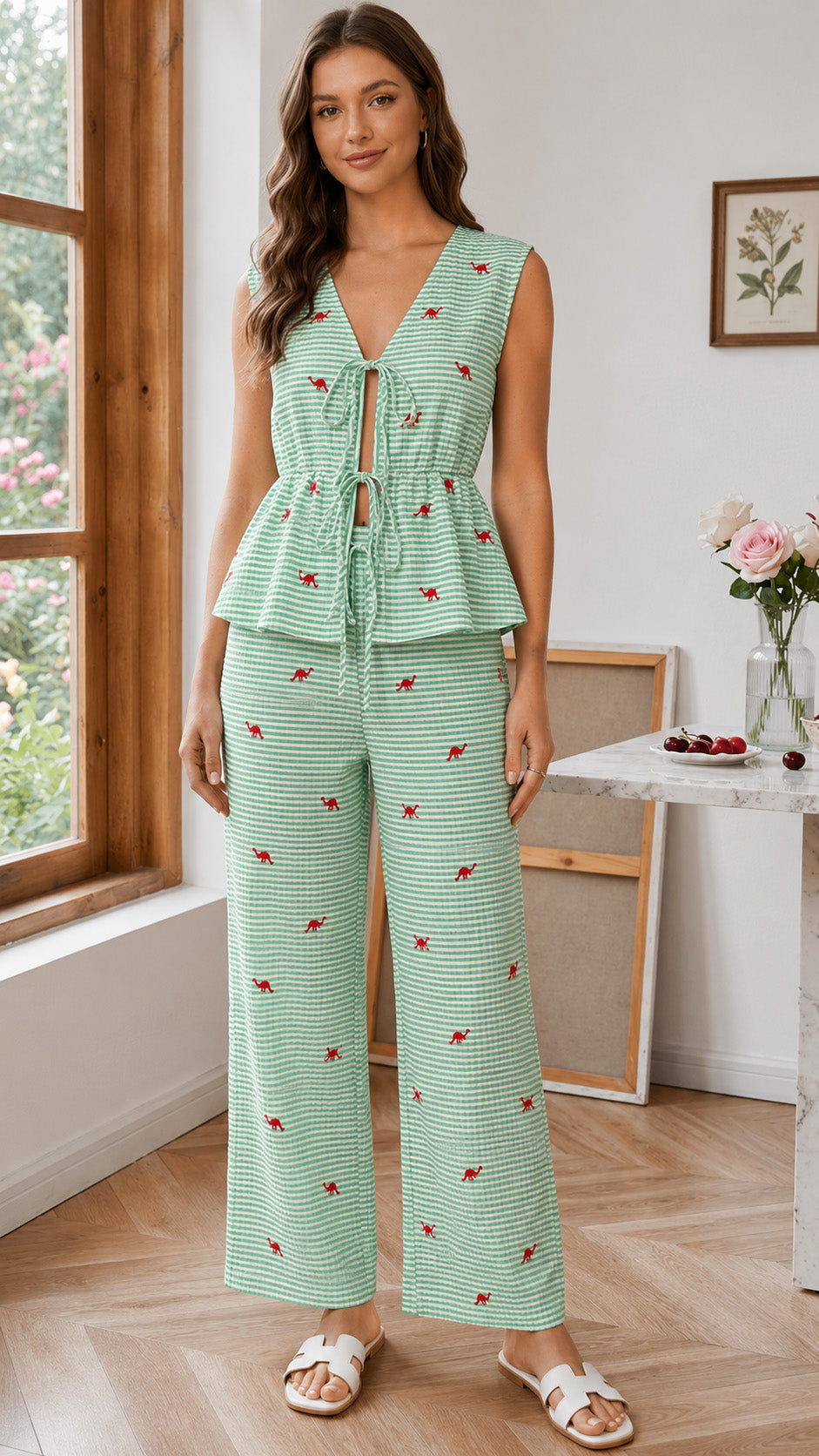 Woman wearing a green patterned jumpsuit standing in a room with a window and table.