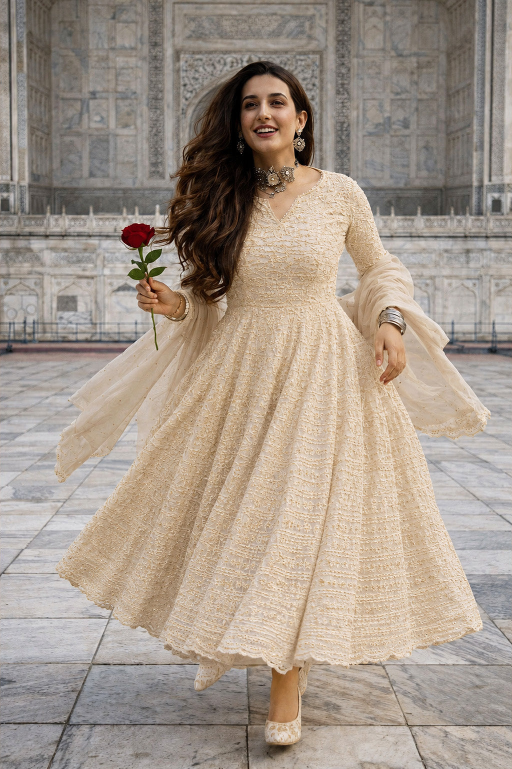 Woman in a beige dress holding a red rose in front of a stone building.