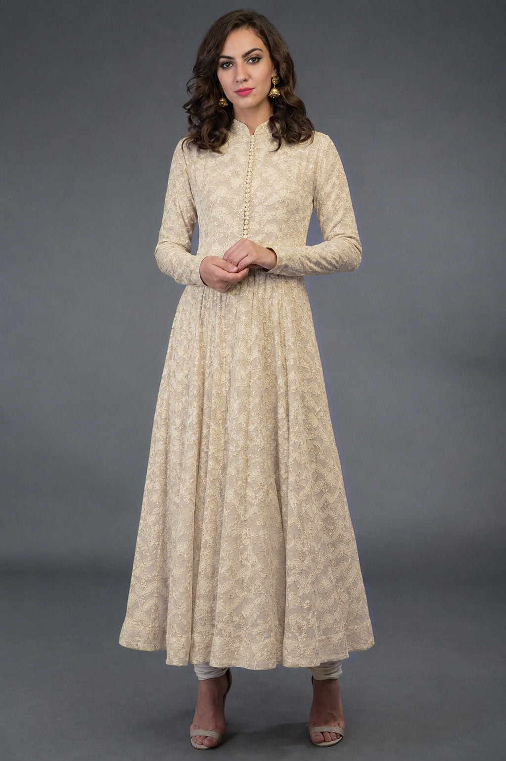 Woman wearing a long beige dress with floral patterns against a gray background