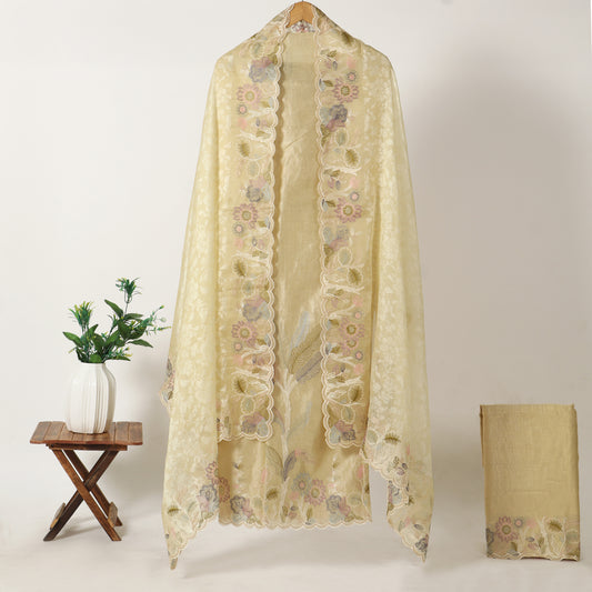 A cream-colored sheer embroidered shawl or scarf draped over a hanger, displayed next to a small wooden side table with a white vase of green leaves and a folded matching fabric piece on a light beige background.