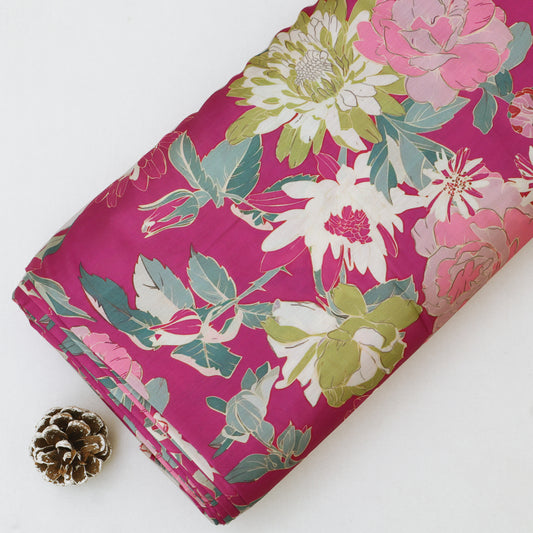 A folded piece of fabric with a vibrant magenta floral print, featuring large white, pink, and green flowers, displayed on a clean white background next to a small pinecone.