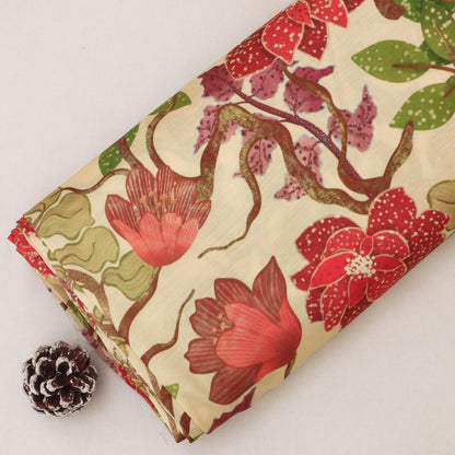 A folded piece of cream-colored fabric with a vintage floral pattern featuring red, pink, and green blossoms, displayed on a light background next to a small pinecone.