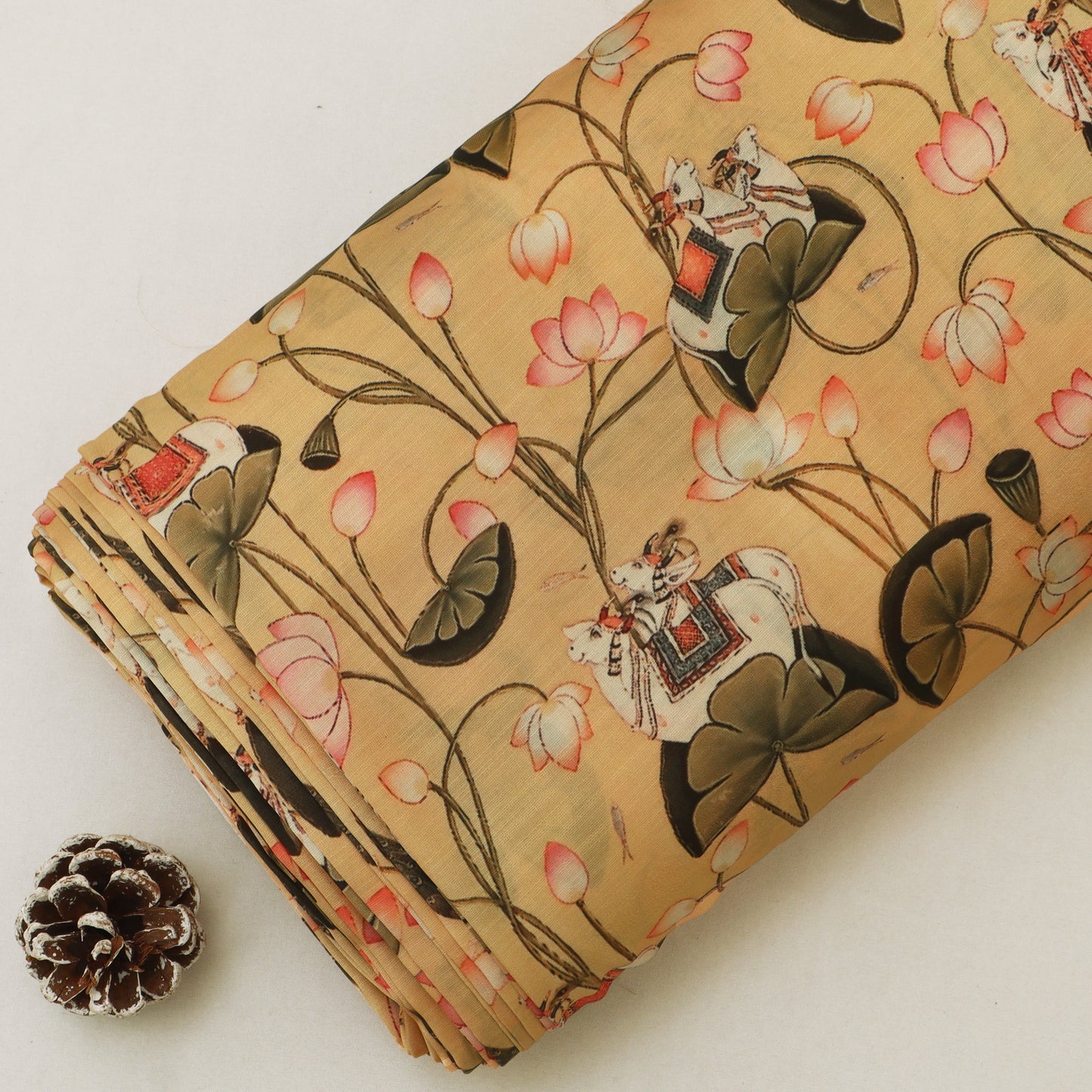 A folded piece of beige fabric with a traditional Chinese print of lotus flowers, lily pads, and figures in boats, displayed next to a small pinecone on a light background.