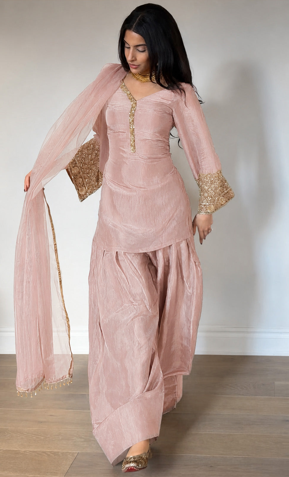Woman wearing a pink traditional outfit with gold details against a plain background