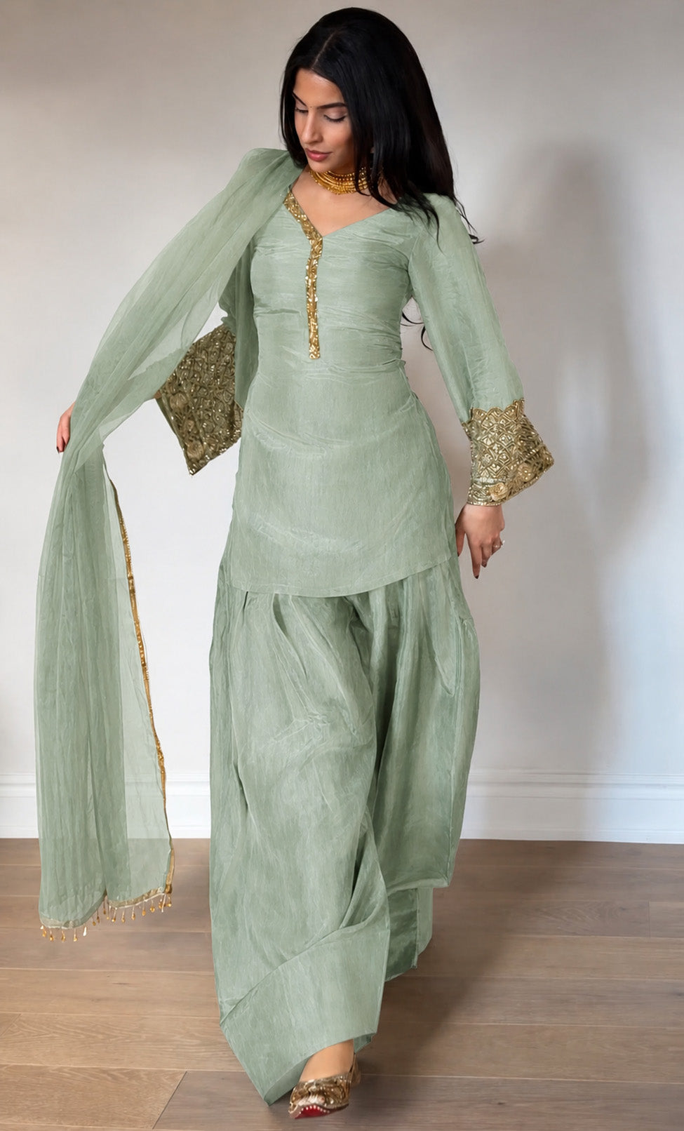 Woman wearing a light green traditional outfit with gold details on a plain background
