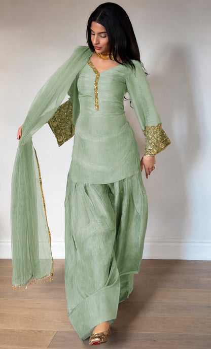 Woman wearing a light green traditional outfit with gold details on a plain background