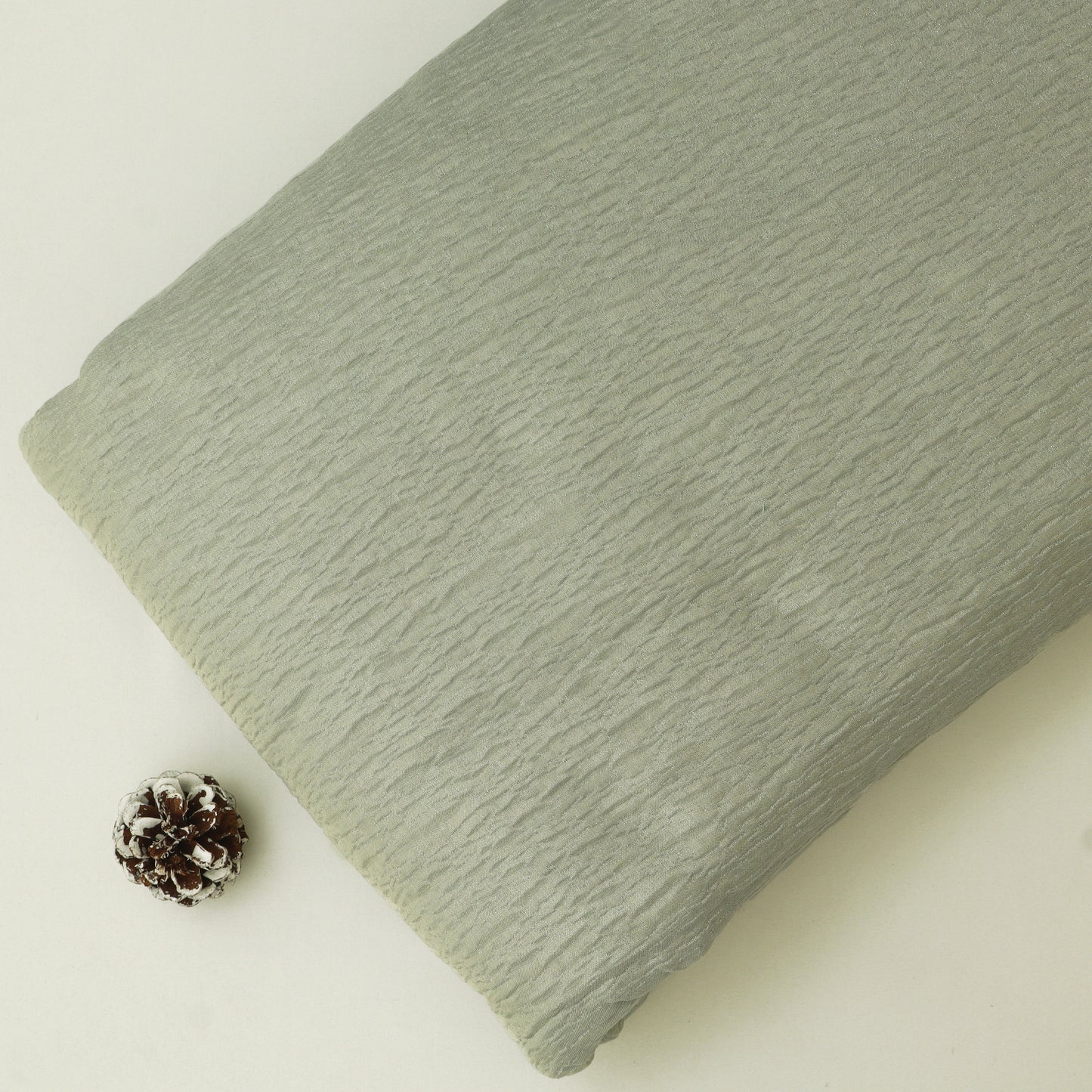 Green textured fabric on a light beige background with a pine cone.