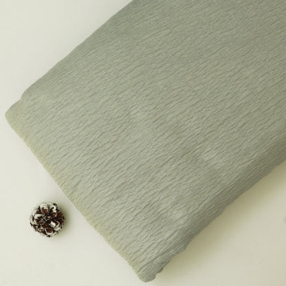 Green textured fabric on a light beige background with a pine cone.