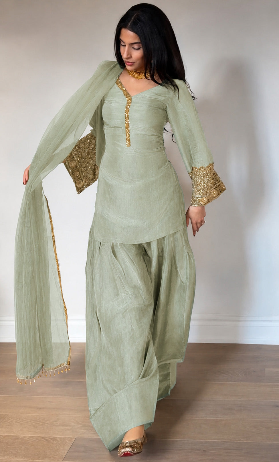 Woman wearing a light green traditional outfit with gold details on a plain background