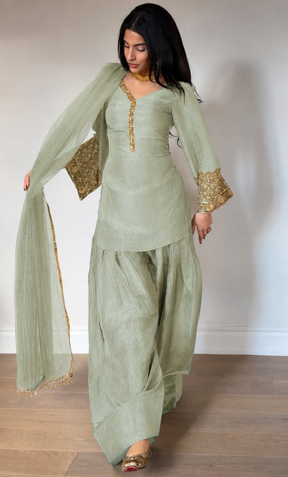 Woman wearing a light green traditional outfit with gold details on a plain background