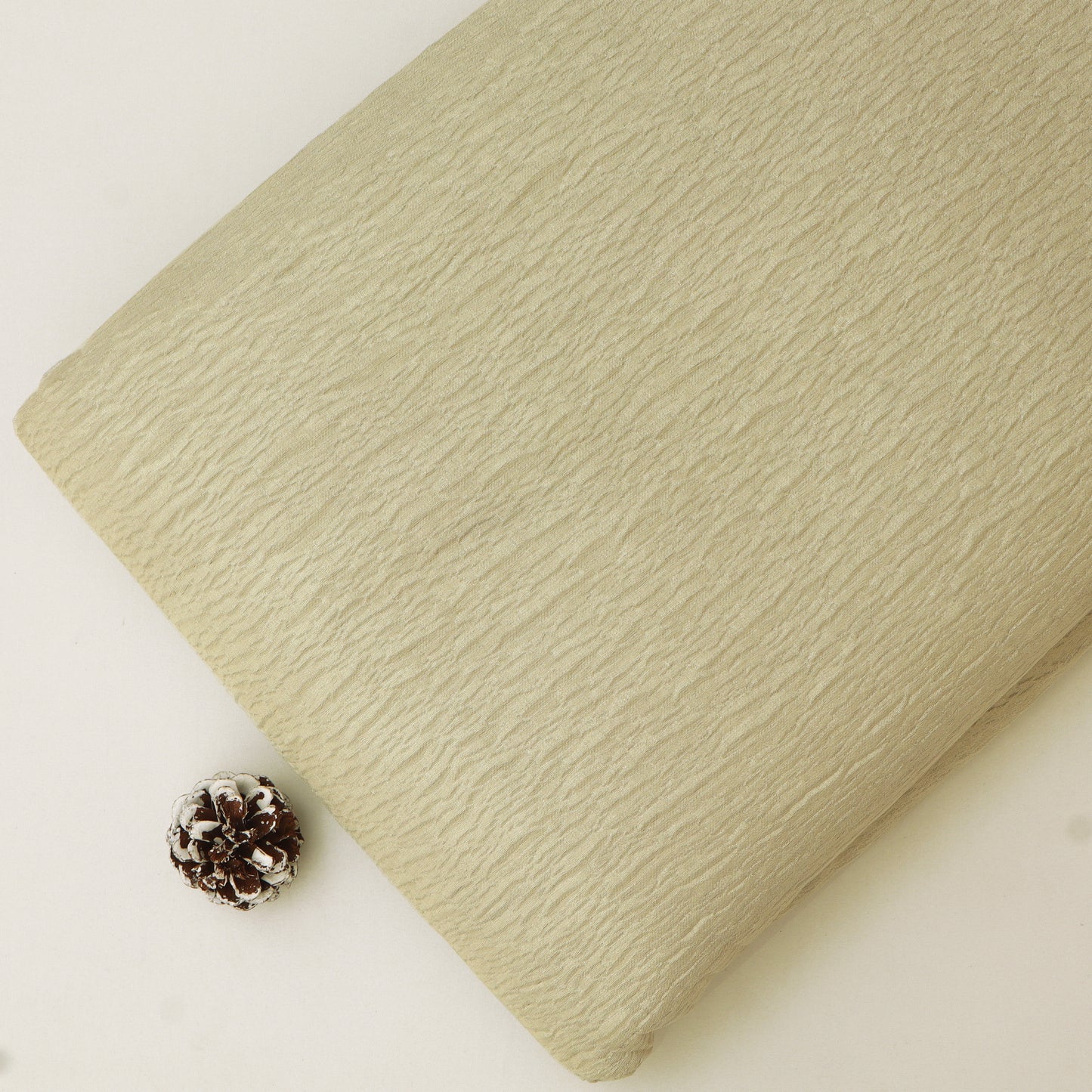 Beige textured fabric roll with a pine cone on a white background