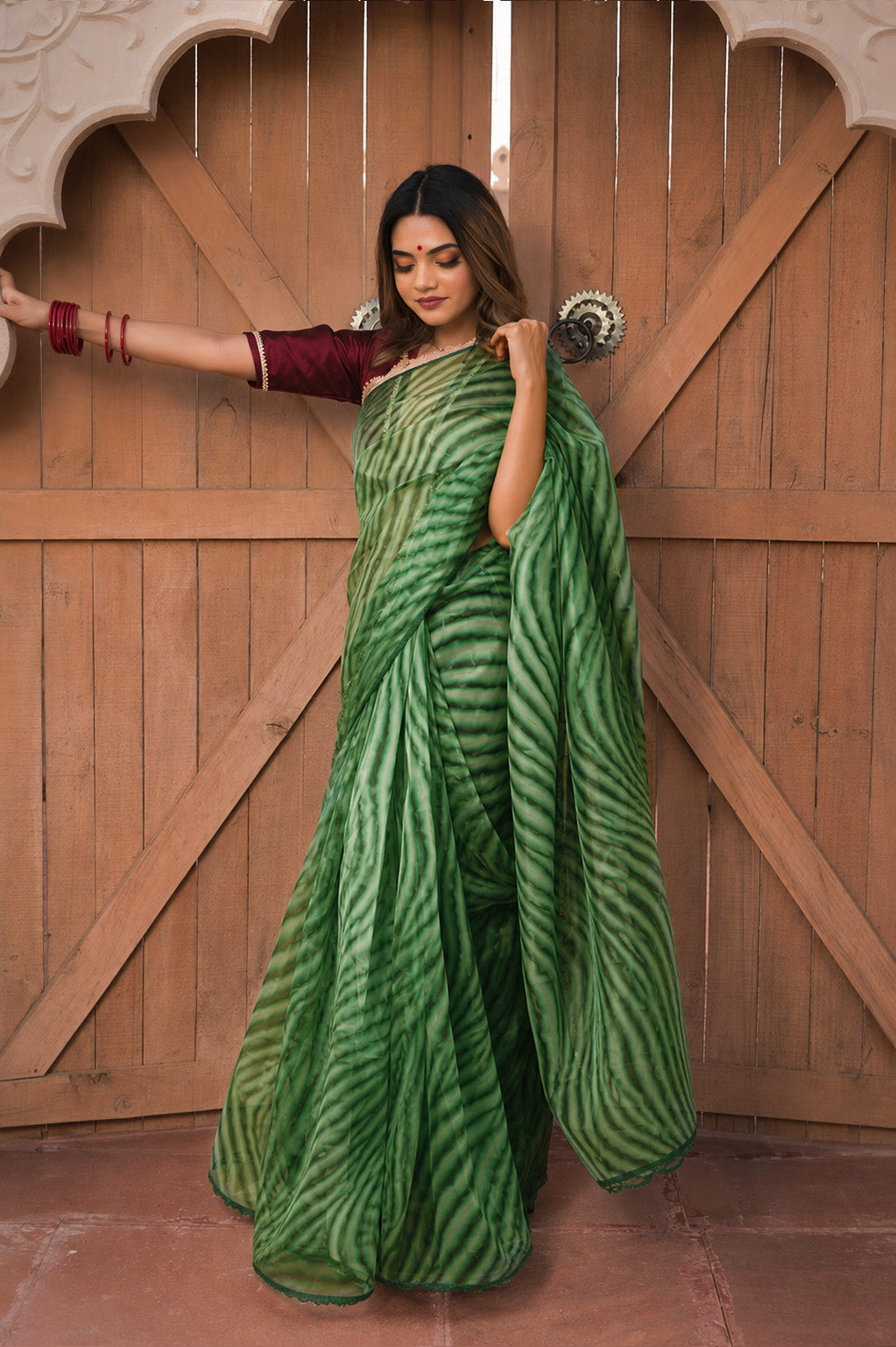Woman in a green saree with a pattern standing in front of a wooden door.