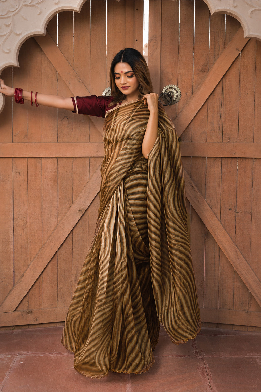 Woman in a zebra-striped saree standing in front of a wooden door.