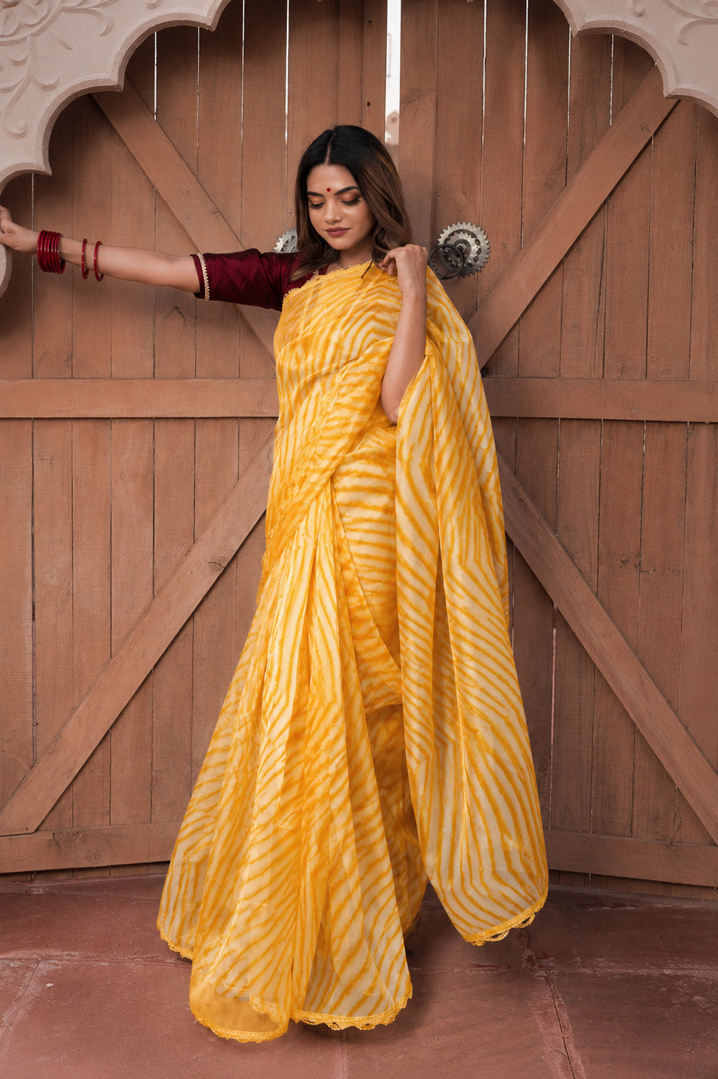 Woman in a yellow saree standing in front of a wooden door