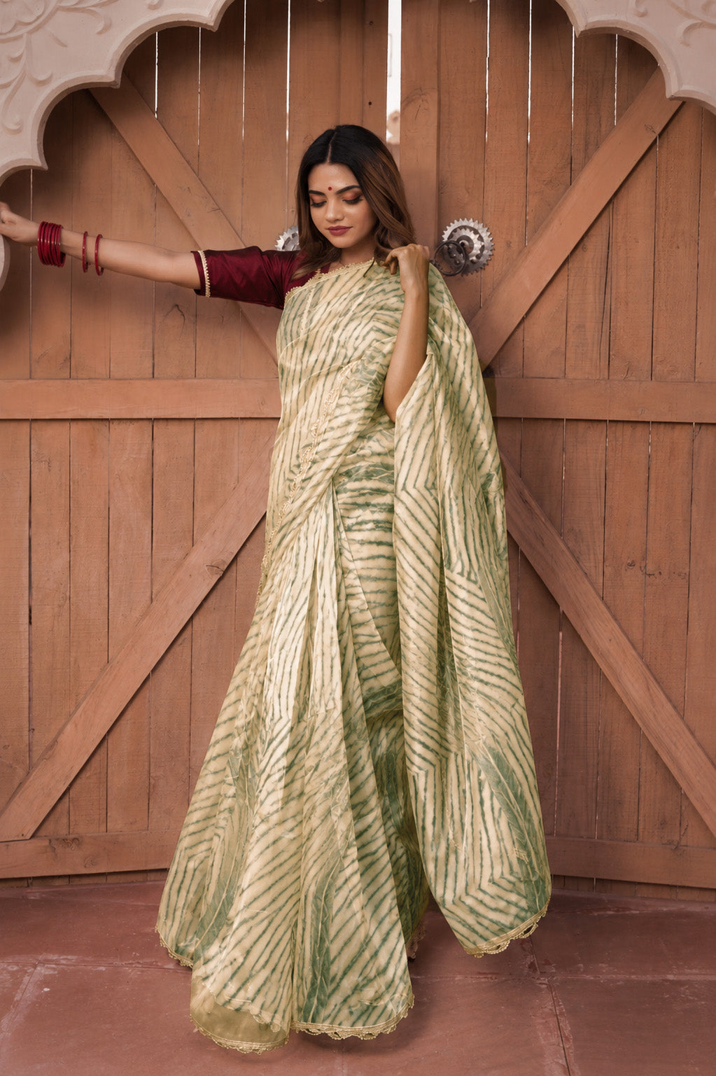 Woman in a green and white saree standing in front of a wooden door.