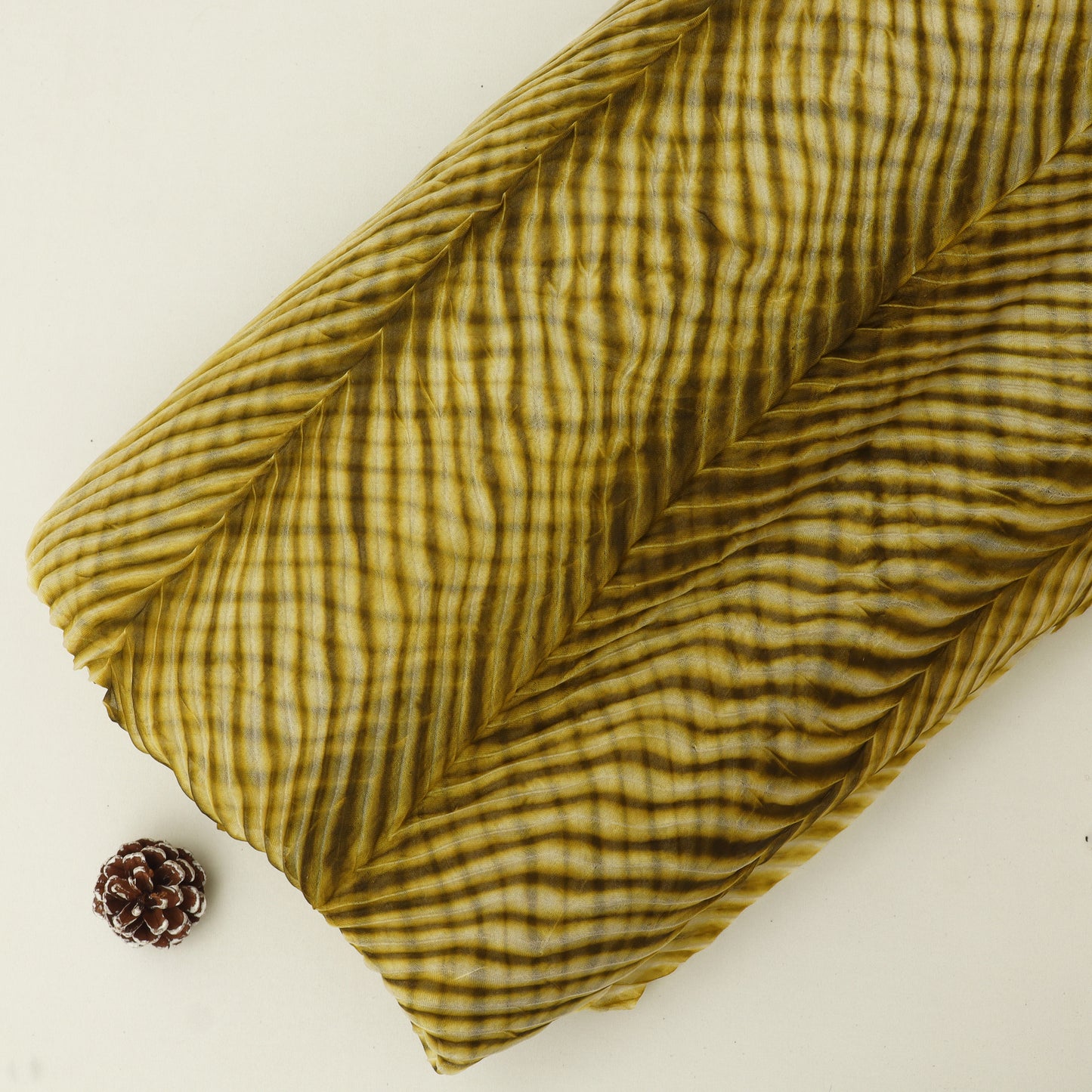 Folded green fabric with a pine cone on a beige background