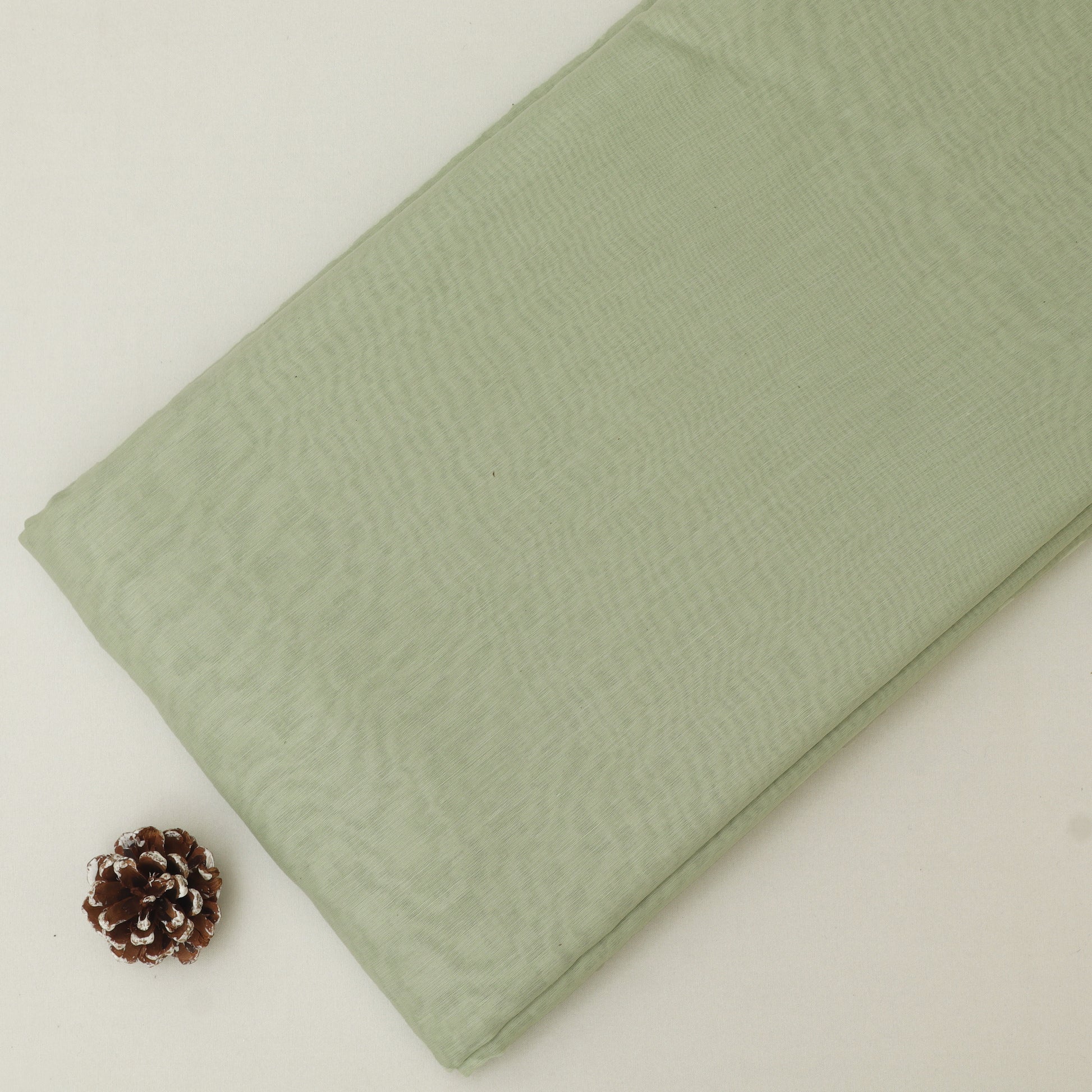Green fabric with a pine cone on a light beige background