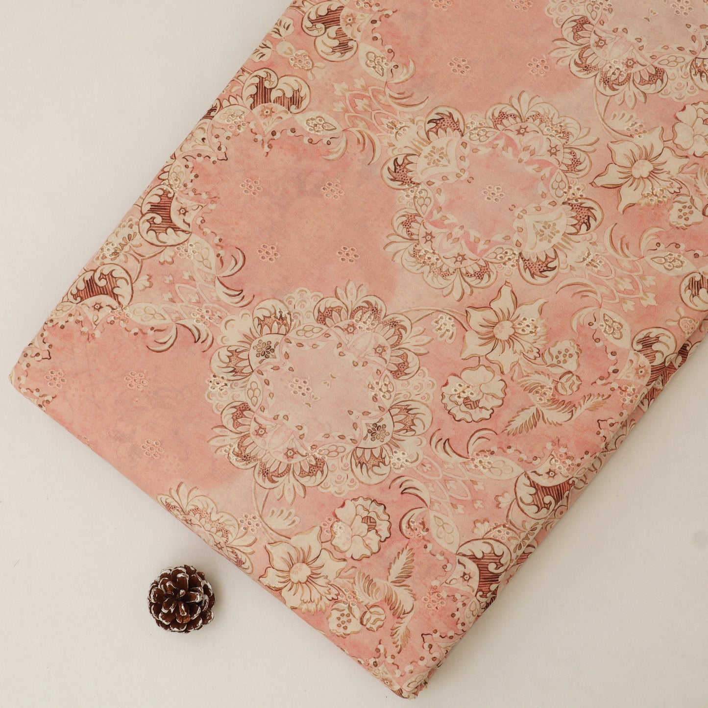 Pink floral patterned fabric on a white background with a pine cone.