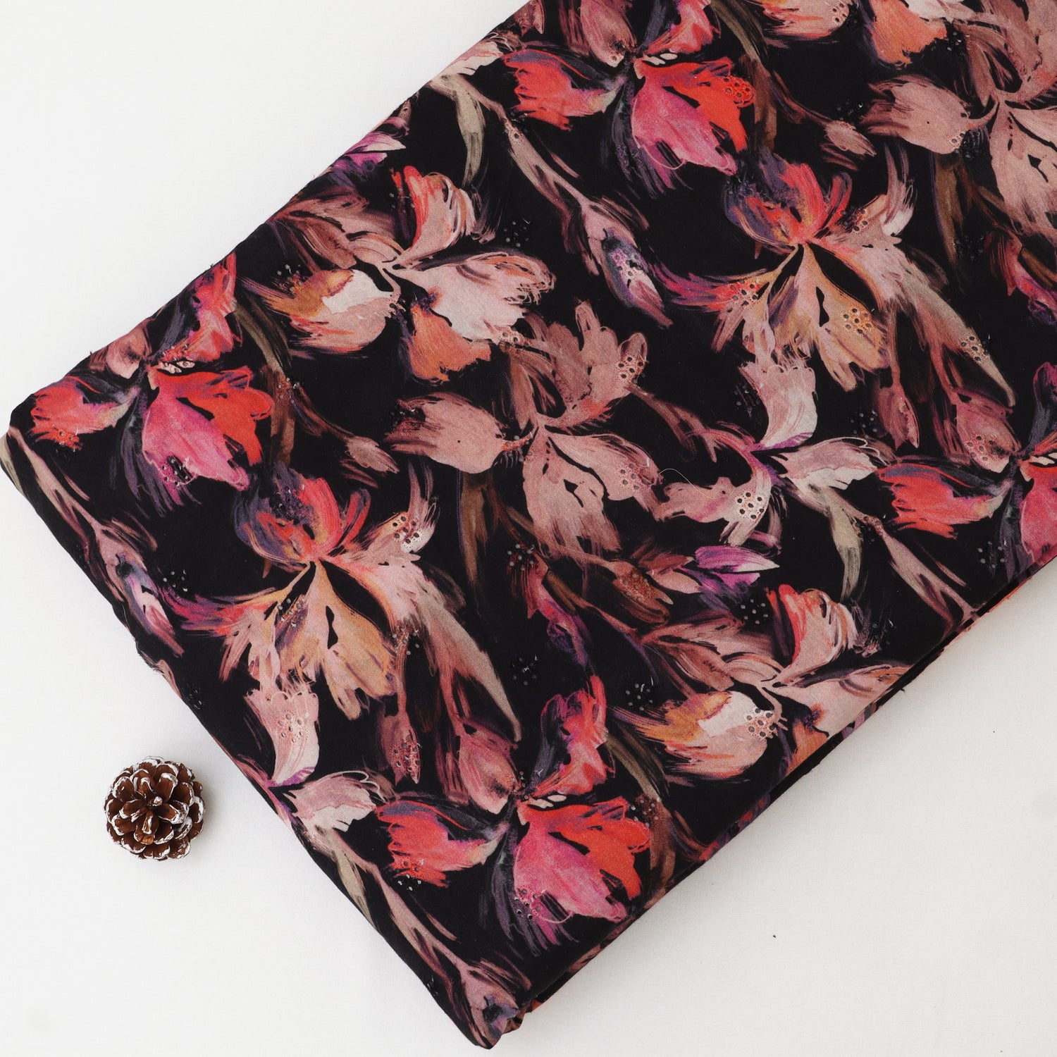 Floral fabric with pink and red flowers on a black background, placed on a white surface.