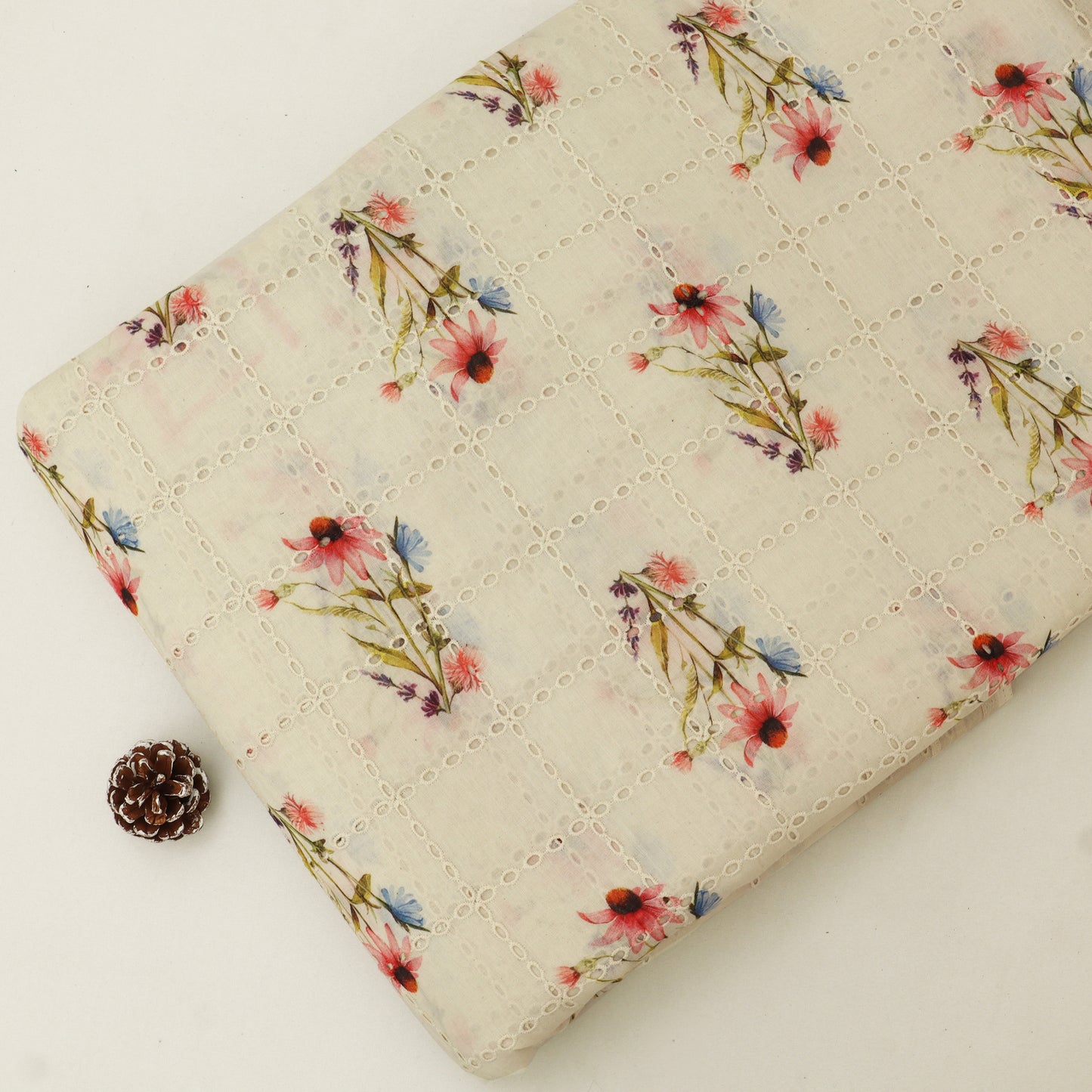 Floral-patterned quilt on a white background with a pine cone.