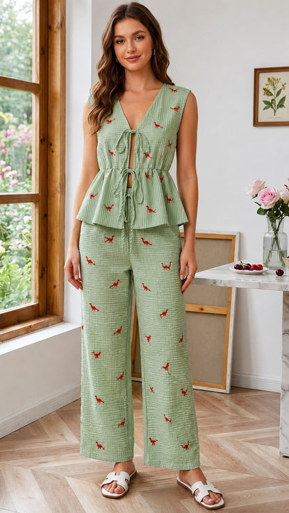 Woman wearing a green patterned jumpsuit standing in a room with a window and table.