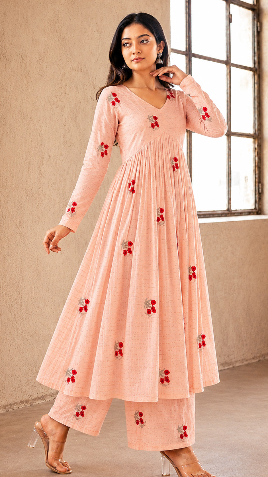 Woman wearing a peach-colored dress with red floral patterns in a room with a window.
