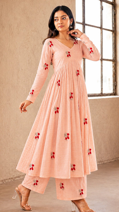 Woman wearing a peach-colored dress with red floral patterns in a room with a window.