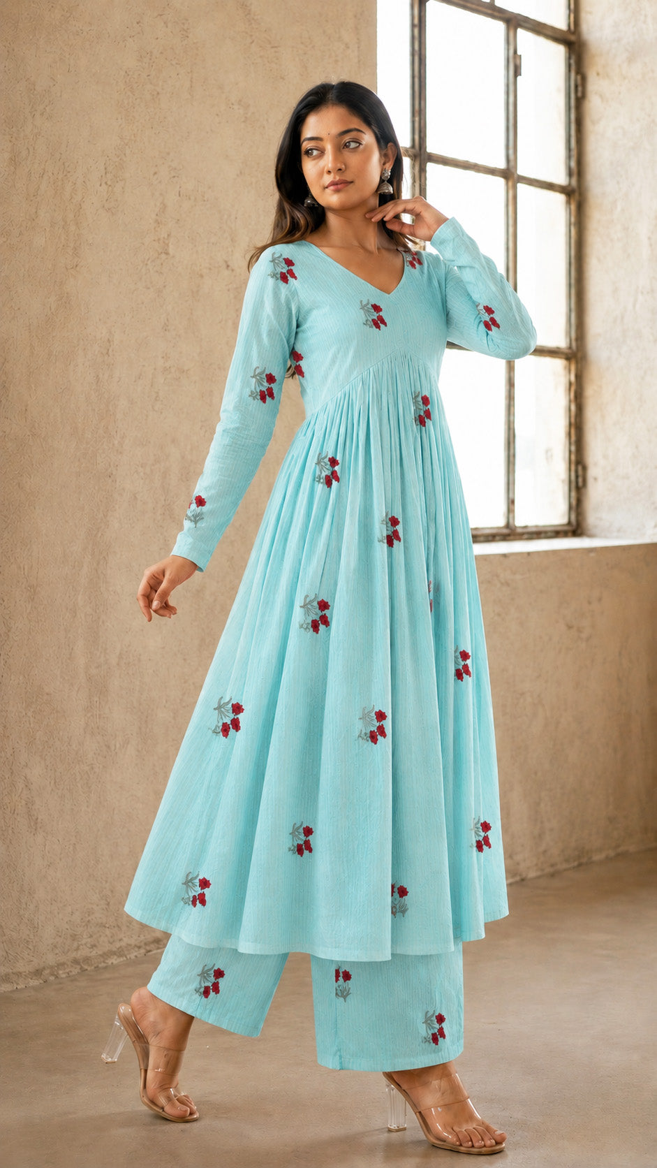 Woman wearing a light blue dress with floral embroidery in a room with large windows.