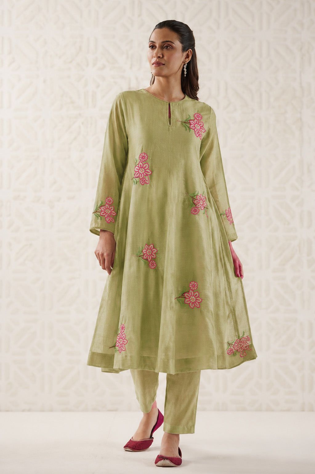 Woman wearing a green embroidered outfit with pink flowers on a light background