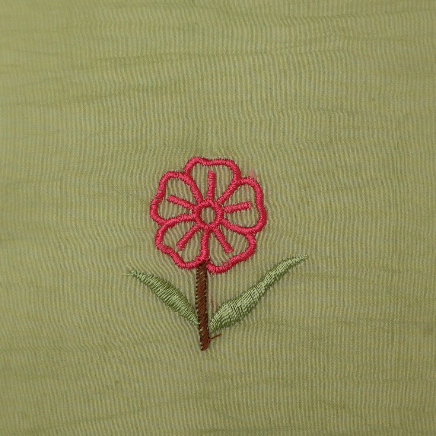 Embroidered pink flower with green leaves on a beige fabric background