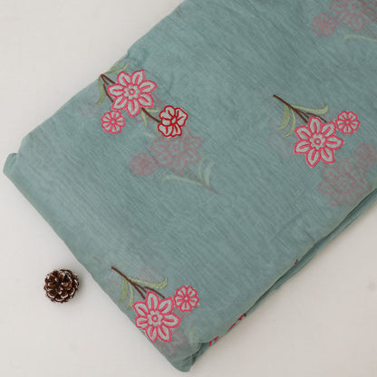 Folded fabric with pink floral patterns on a light blue background, accompanied by a pine cone.
