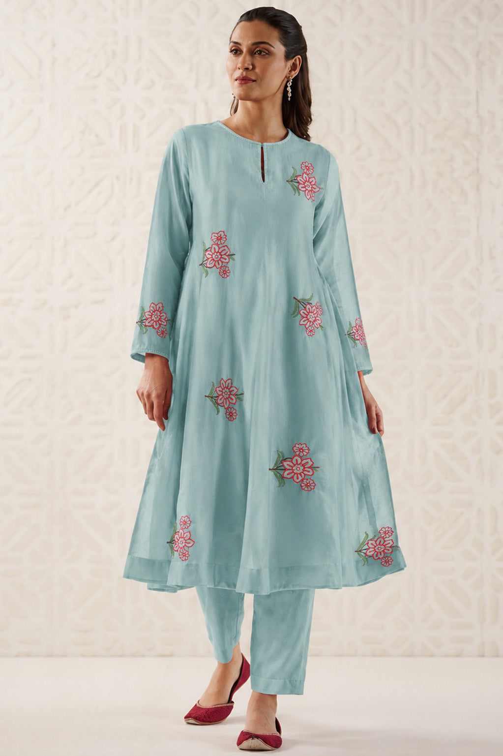 Woman wearing a light blue embroidered outfit on a textured white background
