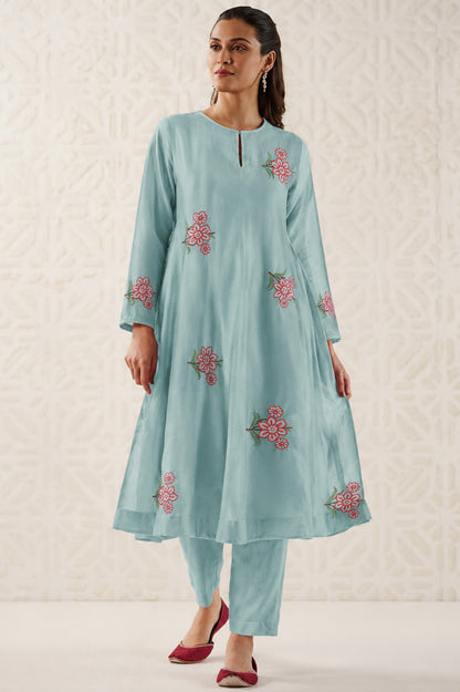 Woman wearing a light blue embroidered outfit on a textured white background