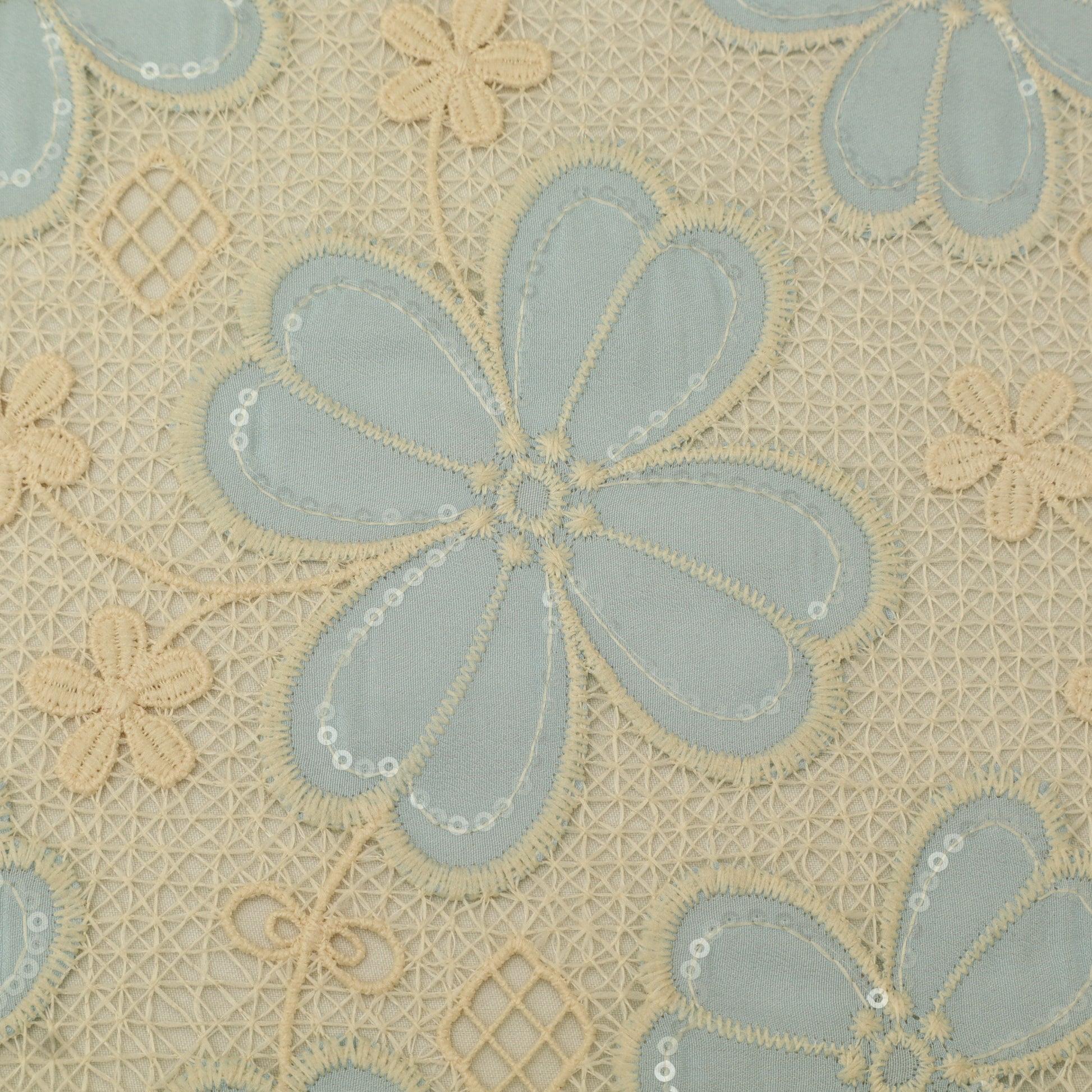 Close-up of floral embroidery pattern with blue and beige flowers on a textured fabric background.