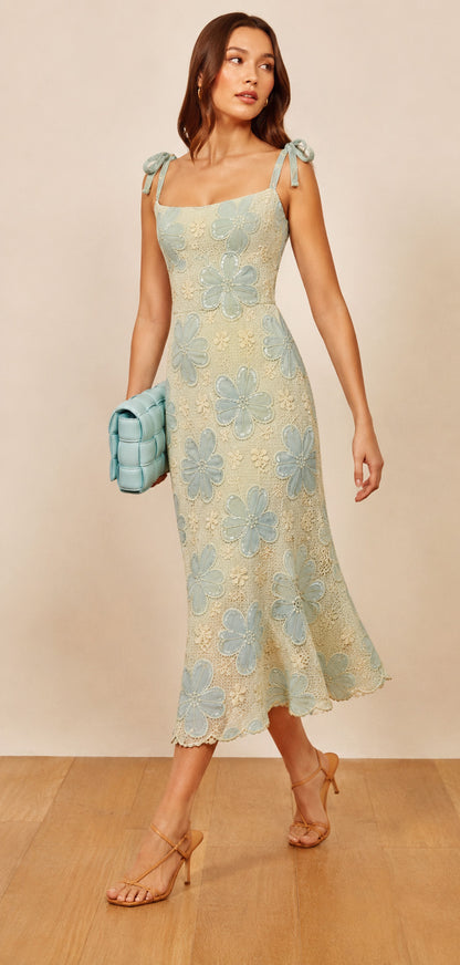 Woman wearing a floral dress holding a clutch against a beige background