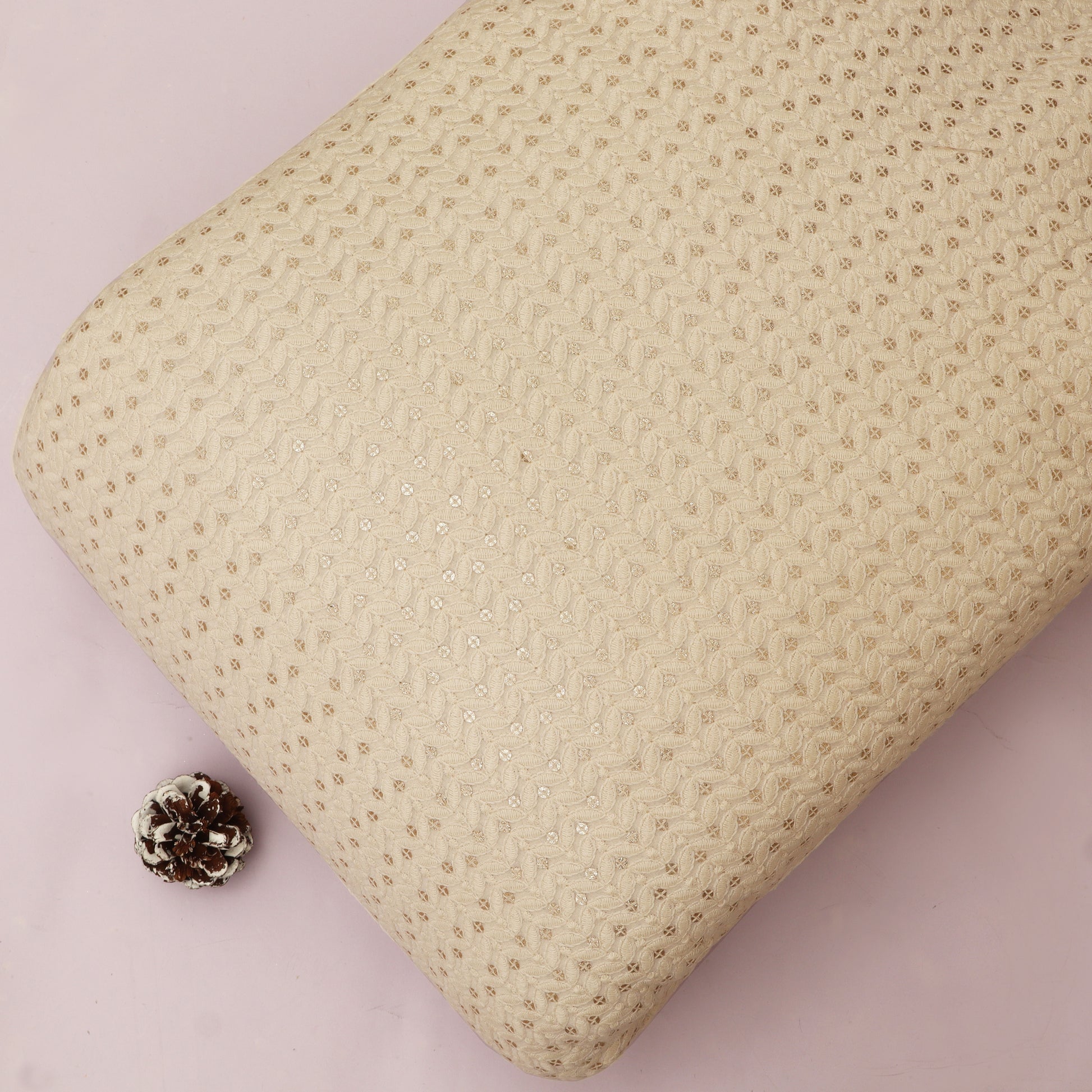 Textured beige pillow with a small decorative pine cone on a pink background