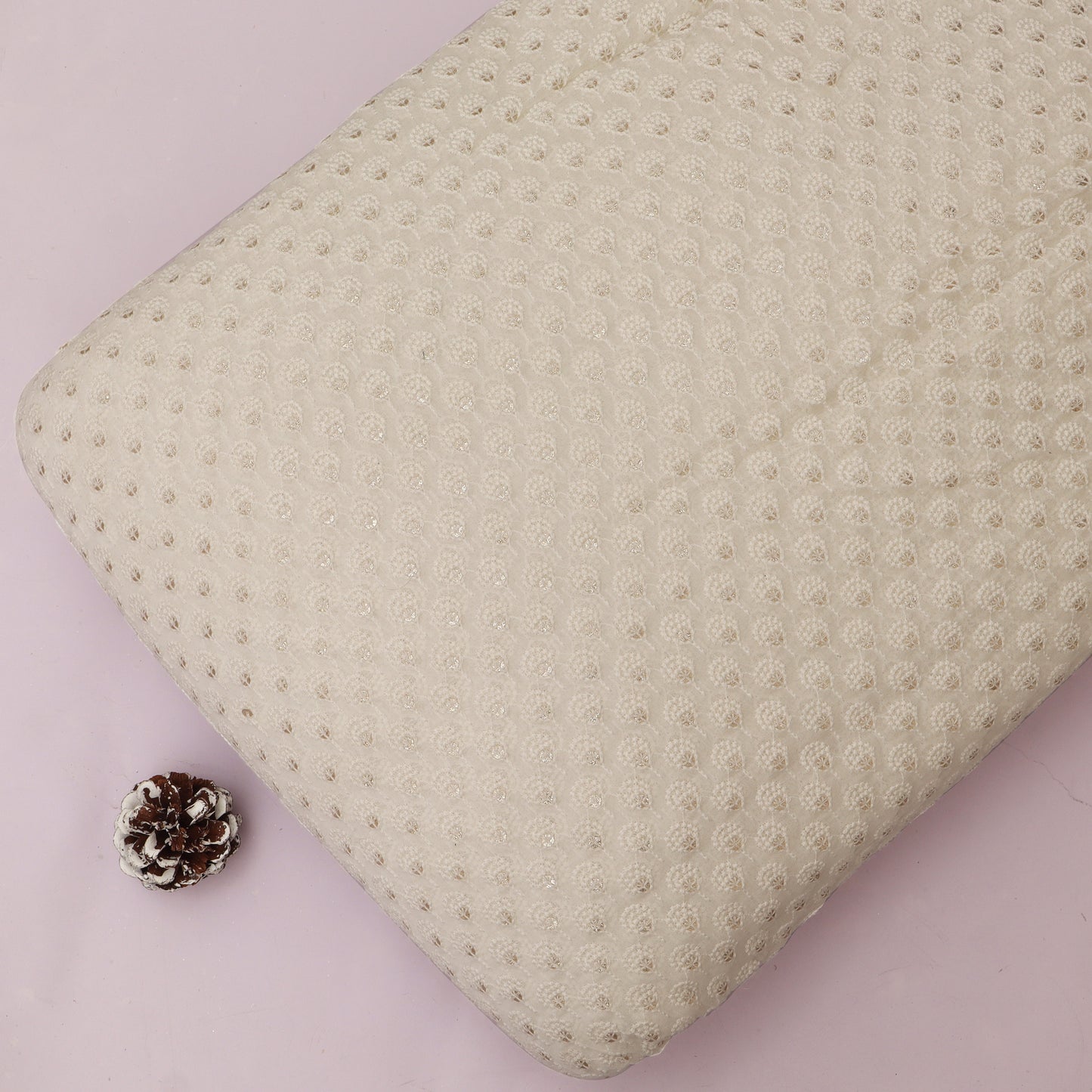 Textured beige pillow on a pink background with a pine cone
