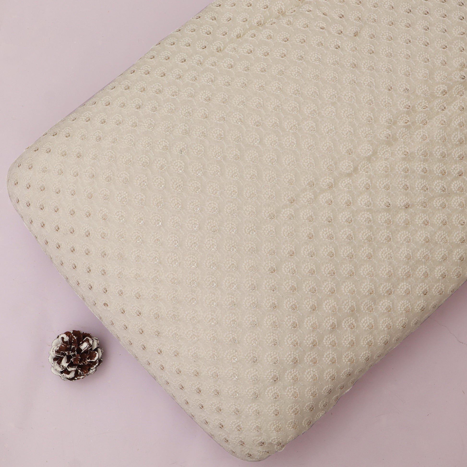 Textured beige pillow on a pink background with a pine cone