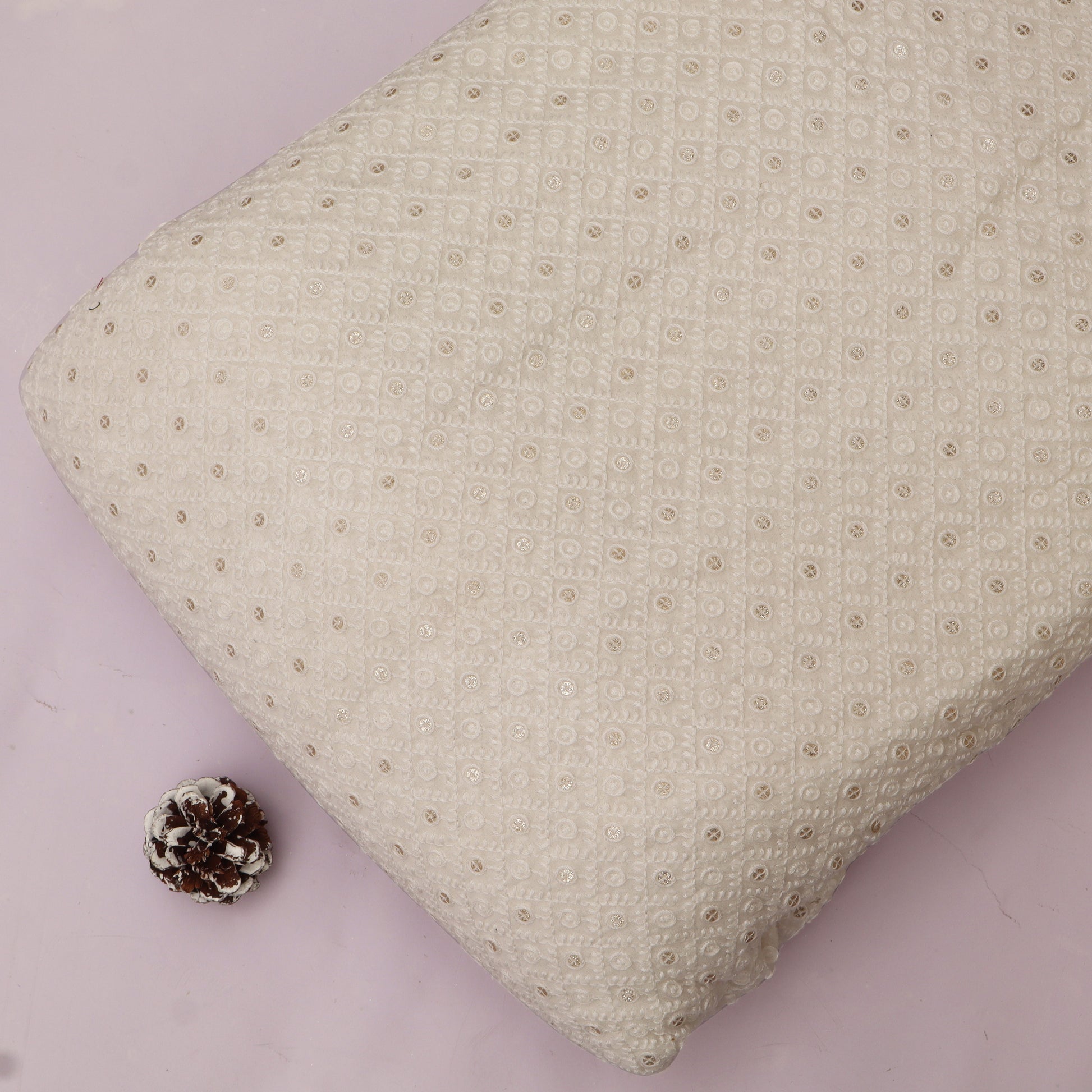 Textured beige pillow with a small pine cone on a White background