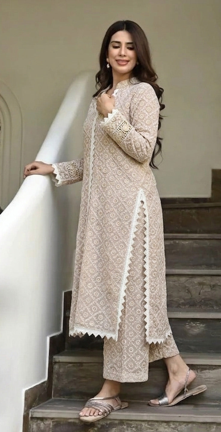 Woman in a beige embroidered outfit standing on steps indoors