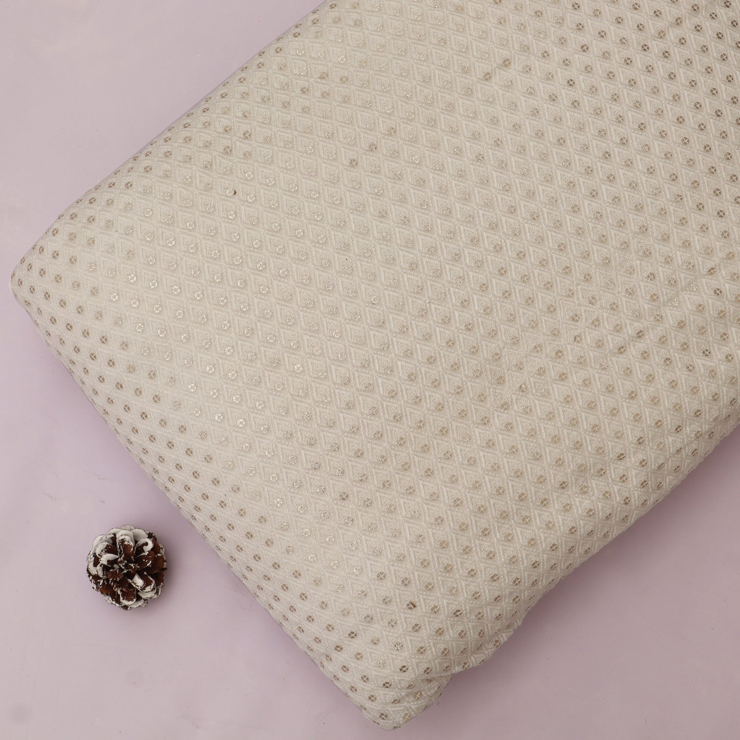 Textured beige pillow on a pink background with a pine cone