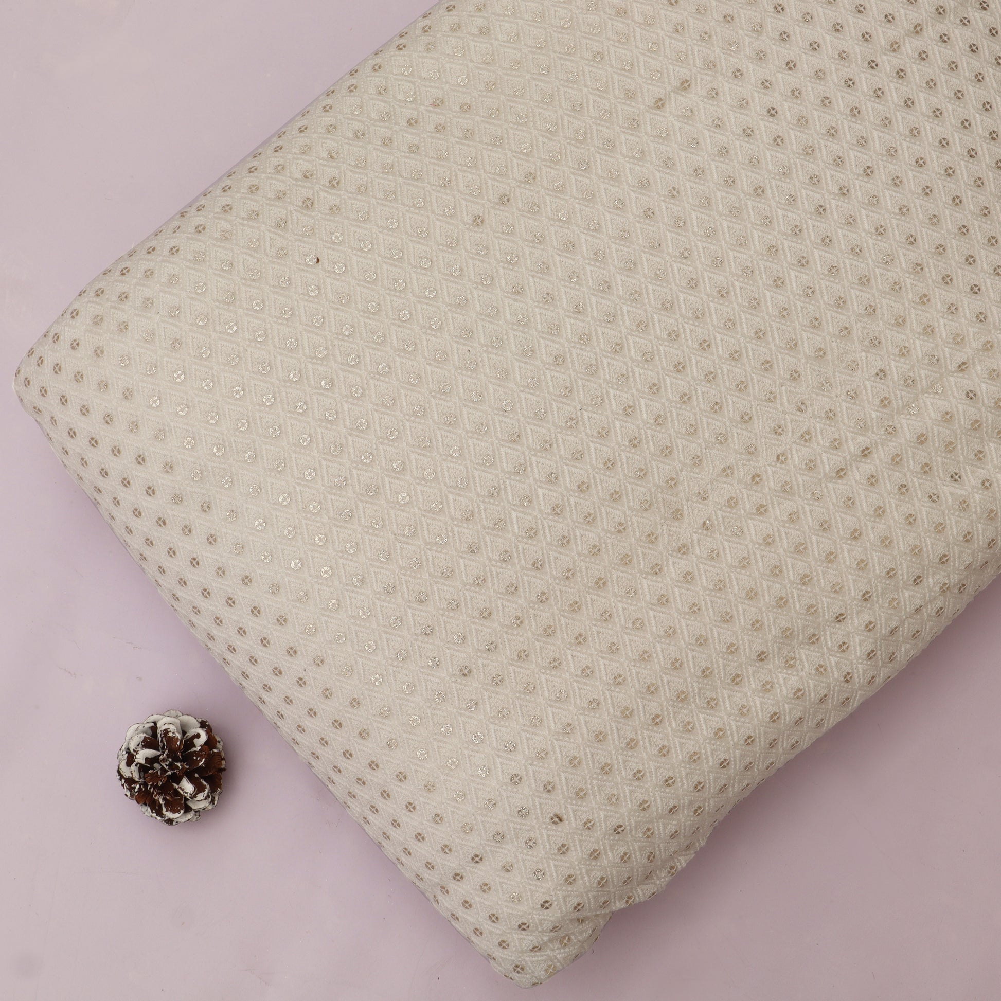 Textured beige pillow on a pink background with a pine cone
