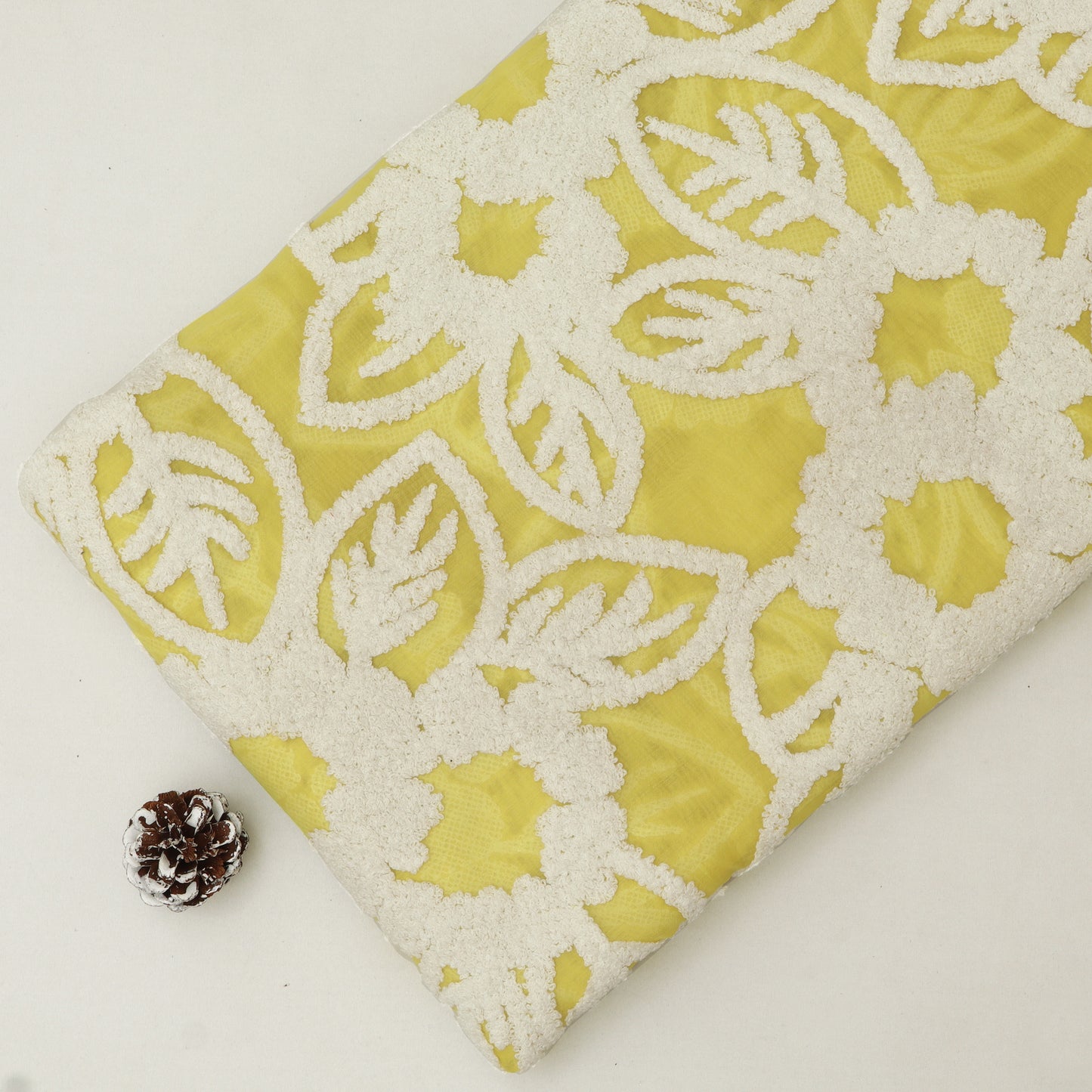 Yellow fabric with white lace pattern and a pine cone on a light background