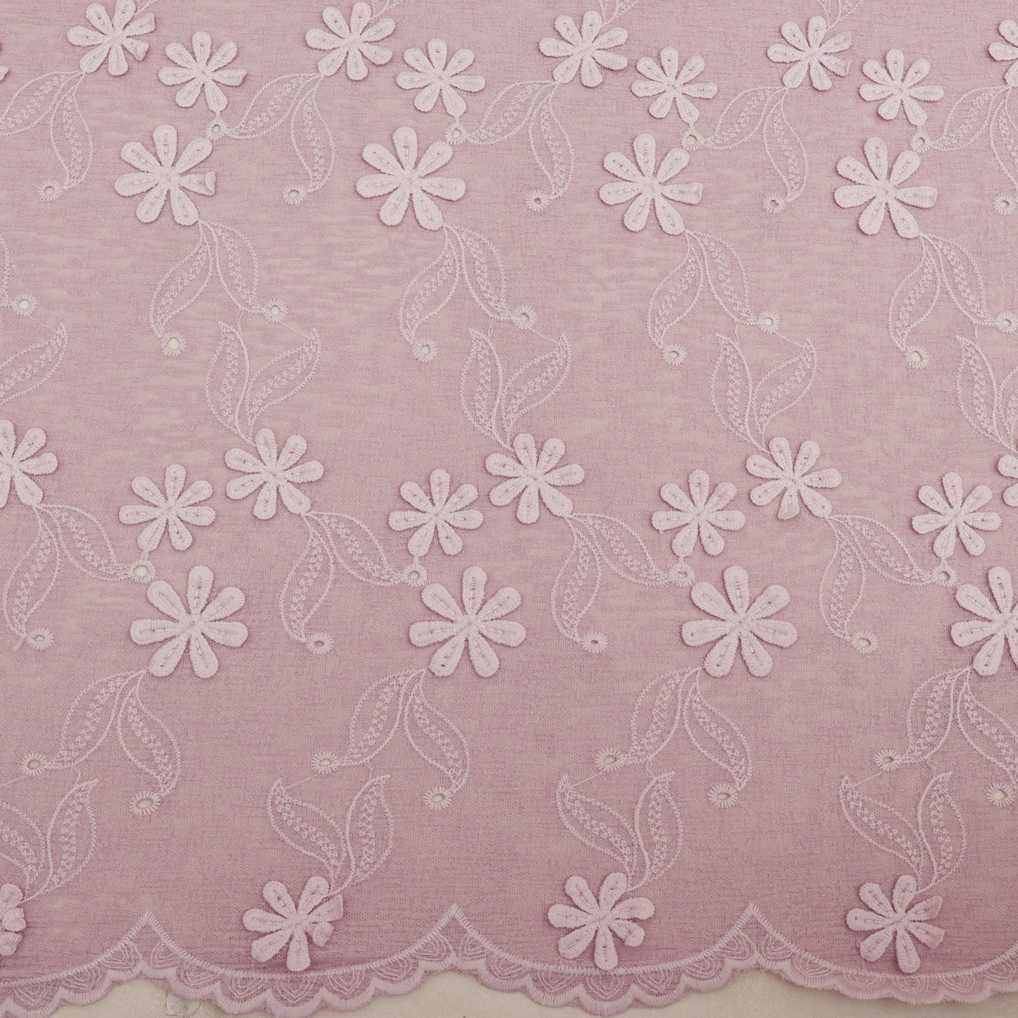 Embroidered lace fabric with white floral patterns on a pink background