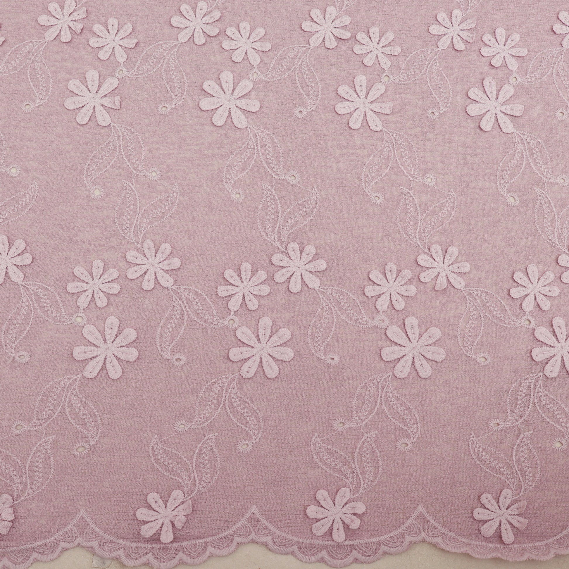 Embroidered lace fabric with white floral patterns on a pink background