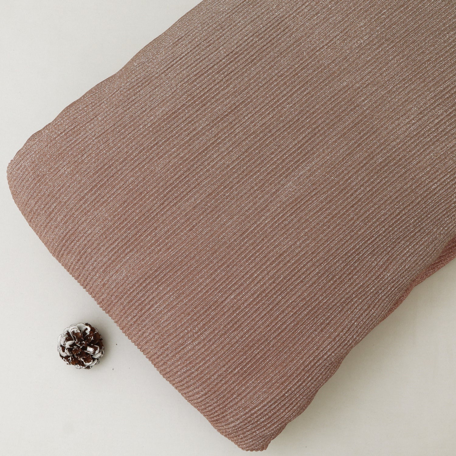 Brown textured fabric on a light background with a pine cone