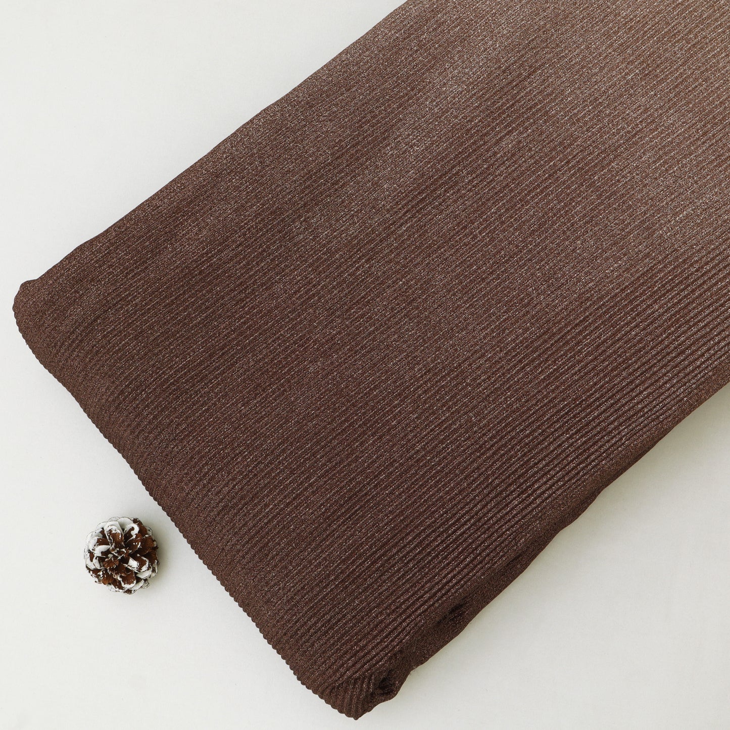 Brown fabric roll on a white background with a pine cone