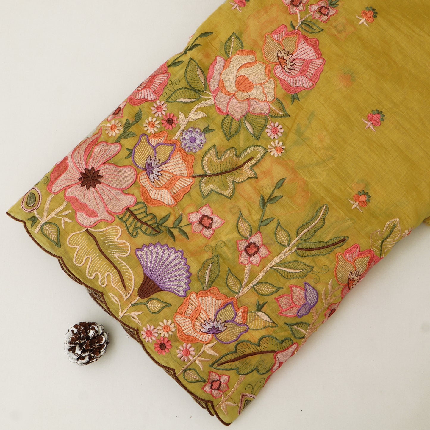 Floral-patterned fabric with pink and green flowers on a yellow background, next to a pine cone.