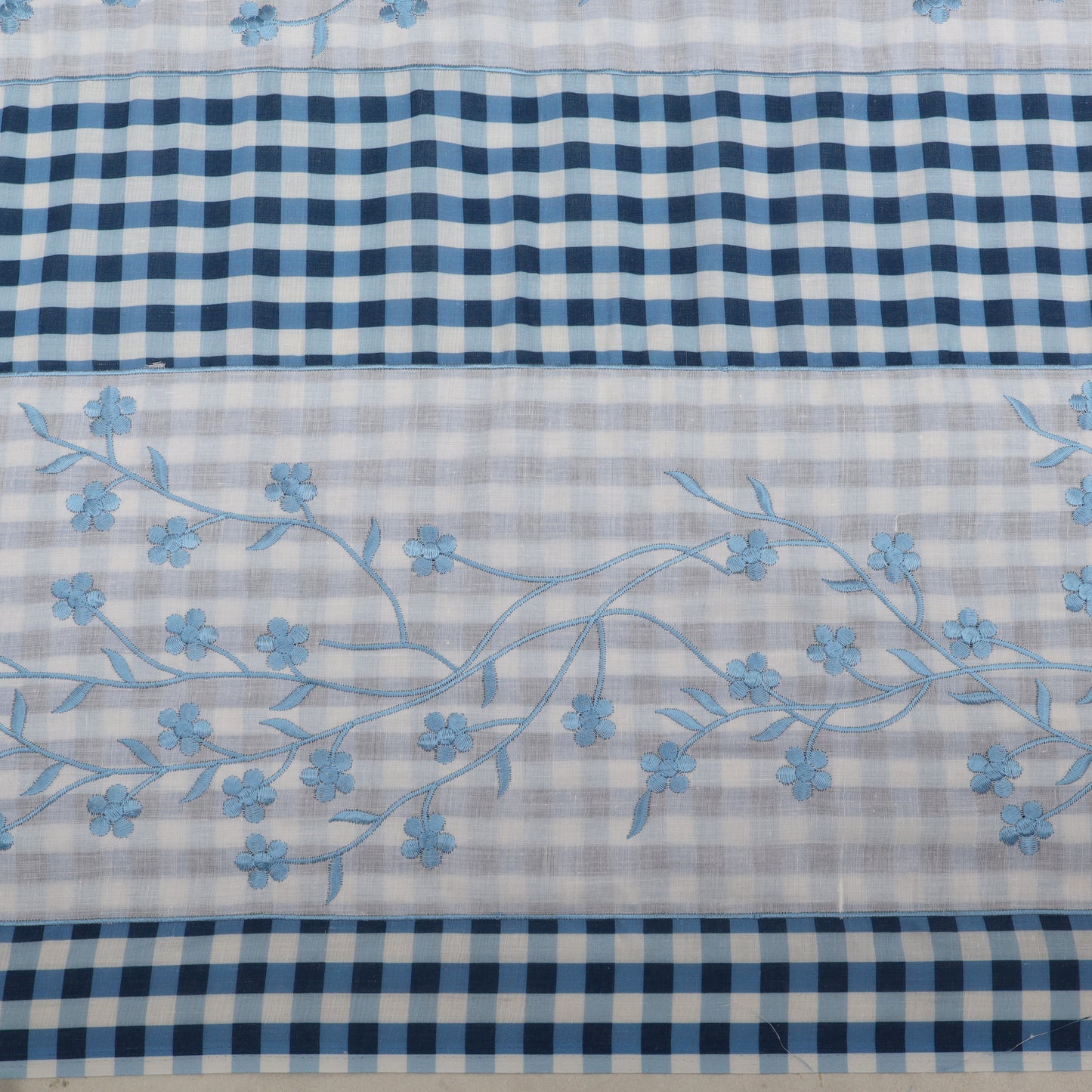 Fabric with blue floral embroidery on a checkered pattern background
