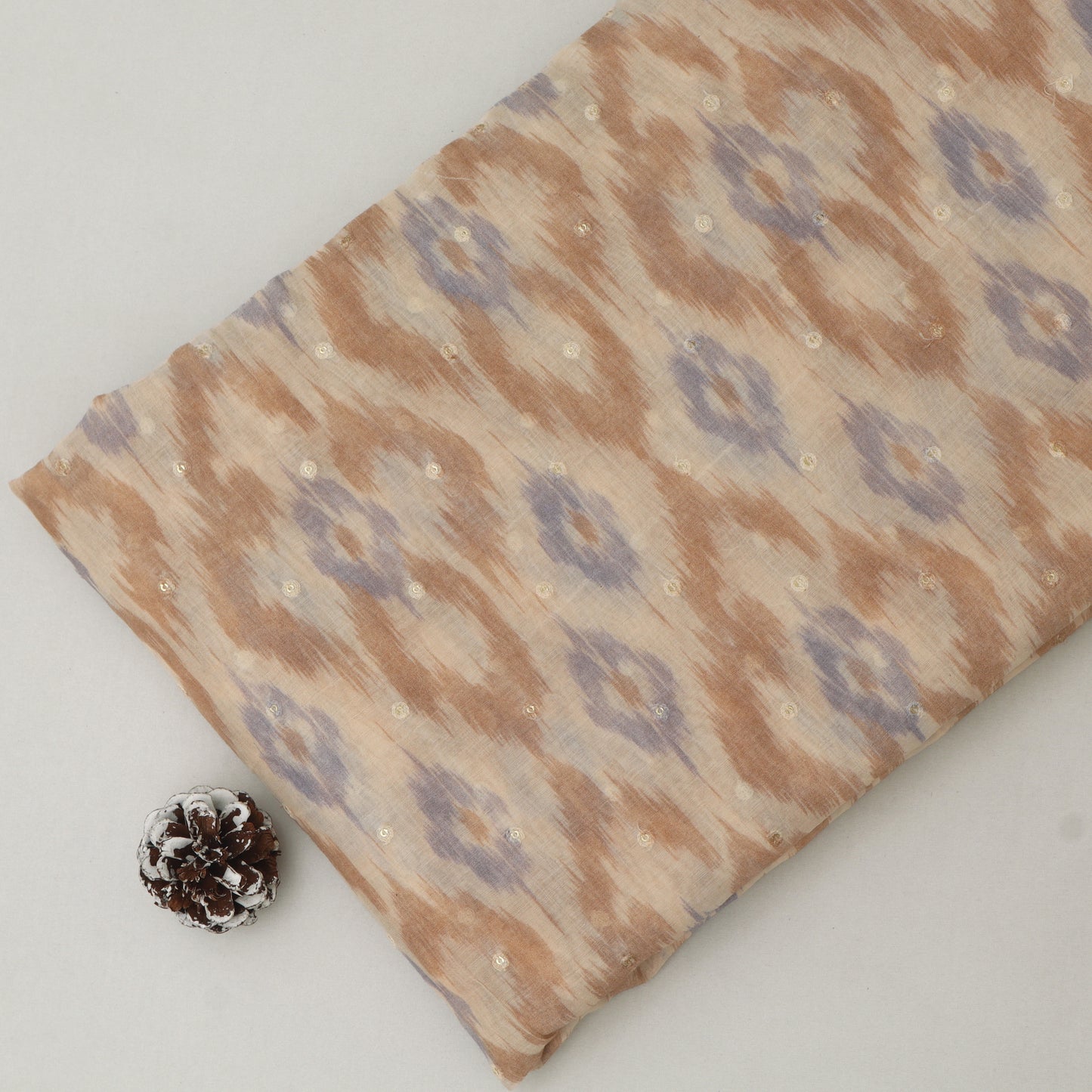Fabric with a pattern next to a pine cone on a white background